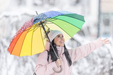 Happy woman holding umbrella on the cold snowy day snowflakes fall on her hand.の写真素材
