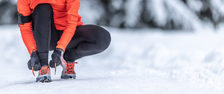 A close-up view of a female runner tying her shoelaces before training on the snow in the winter season.の写真素材