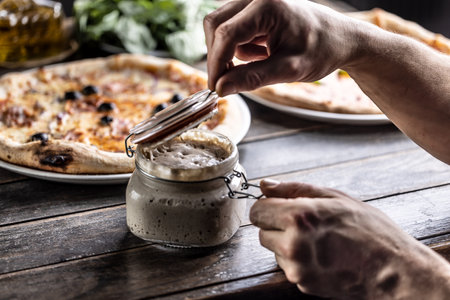 Cook's hands open a jar of rye sourdough, in the background a pizza made with sourdough.の写真素材
