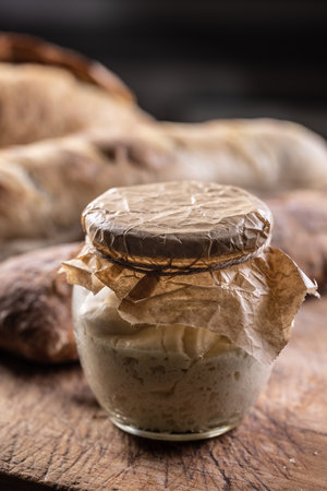 Rye sourdough ripened in a jar together with fresh bread on a cutting board.の写真素材