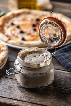An open jar with a yeast starter and a sourdough pizza in the background.の写真素材