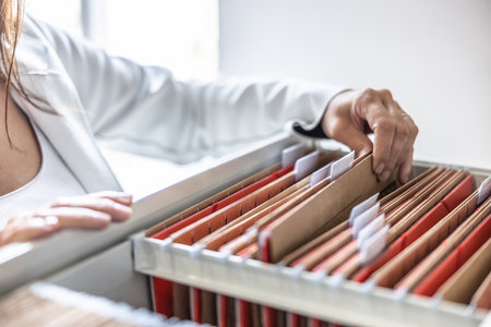 The clerk is leafing through stored folders, looking for a file or document. Concept of data storage, filing cabinet and business administration.の写真素材
