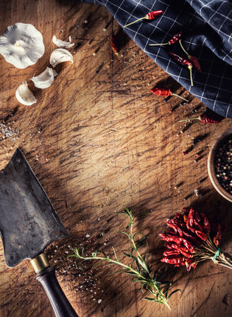 An old cutting board with a butcher's cleaver, pepper, chili peppers, garlic, salt and rosemary on it - Top of view.の写真素材