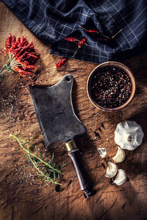An old butchers cleaver on a cutting board surrounded by chili peppers garlic and rosemary - Top of view.の写真素材