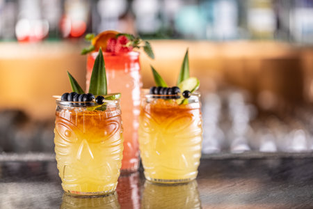 Mai tai cocktails in hawaiian glasses garnished with pineapple, blueberries and strawberries on bar counter.の写真素材