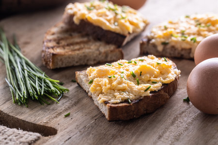 Fresh scrambled eggs spread on a slice of bread with whole eggs and fresh chive on the side.の写真素材