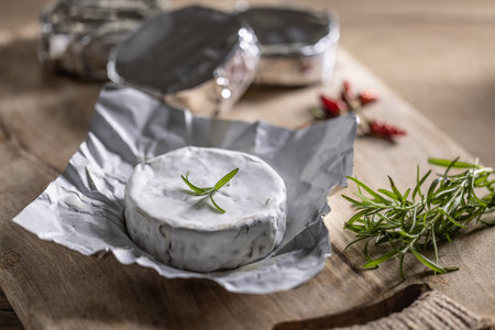 Tinfoiled packages of brie cheese with rosemary and chilli on a cutting board.の写真素材