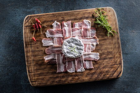 Top view of a wooden board on rustic dark surface with prosciutto slices, camembert cheese, rosemary twig and fresh chillies.の写真素材