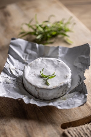 Opened package of brie cheese with a spring of rosemary on top with a rustick background.の写真素材
