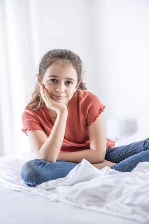 Young and confident pre-teen girl sits and leans on her hand looking into the camera.の写真素材