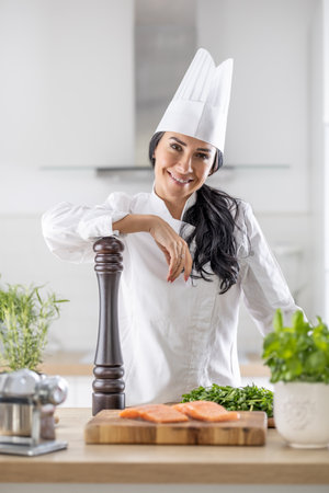 Professional female chef confidently leans on pepper grinder with ingredients for cooking in front of her.の写真素材