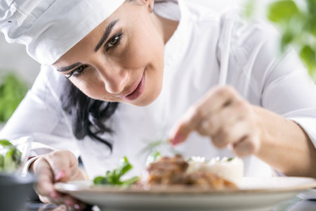 A young female chef finishes the meal with herbs in the restaurant kitchen - Close up.の写真素材