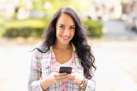 A smiling brunette is writing messages on her mobile phone. A young woman reads received messages and writes back on a smartphone.の写真素材