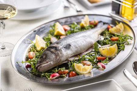 Sea bass raw fish staged on a silver tray on green, red and yellow coloured salad.の写真素材