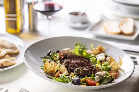 Beef steak sliced on top of mixed salad with greens, physalis, cherry tomatoes served with wine.の写真素材