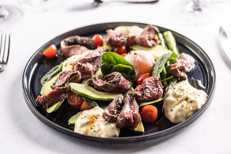 Colorful salad with flank steak filling the dark plate on a restaurant table.の写真素材