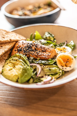 Fresh leaf salad served with avocado, eggs and grilled salmon on the top studded by sesame.の写真素材