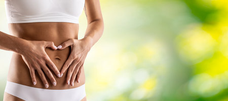 Middle part of female body with heart shape from hands. A woman in underwear symbolizes a healthy lifestyle, a healthy stomach, menstruation or pregnancy. Green natural background.の写真素材