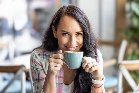 Attractive brunette in a good mood enjoys a cappuccino in a cafe.の写真素材