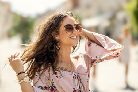 Happy young smiling woman in summer outfit with sunglasses walking in the city with wind blowing her hair.の写真素材