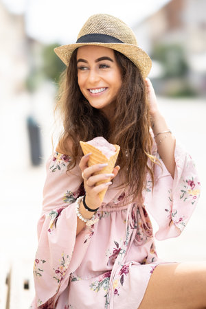 Portrait of a beautiful smiling lady in a summer outfit holding an ice cream on a hot summer day.の写真素材