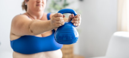 Plus size woman doing exercises with dumbbells, strengthening her body in living room, selective focus.の写真素材
