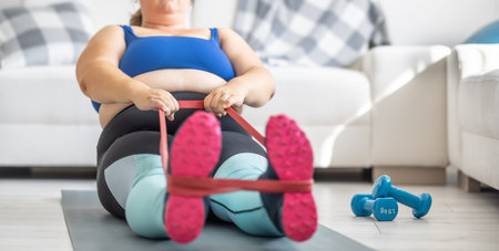Overweight lady doing sports exercise in living room. He lies on the mat and stretches the sports rubbers.の写真素材
