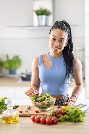 Young African American woman prepares healthy salad, adds tomatoes.の写真素材