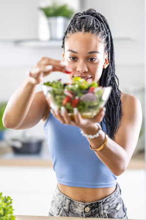 Young African American woman prepares healthy salad, adds tomatoes.の写真素材