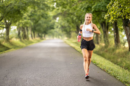 Female runner jogging outside in the park. Young woman runner running with a bottle of water.の写真素材