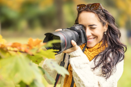 A smiling female photographer takes pictures of autumn leaves with her professional camera.の写真素材