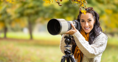 A satisfied photographer is standing behind her camera placed on a tripod, taking autumn photos.の写真素材