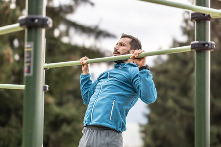 Young man working out calisthenics in an outdoor gym using parallel bars. He does push-ups on the bar. Concept of healthy lifestyle.の写真素材