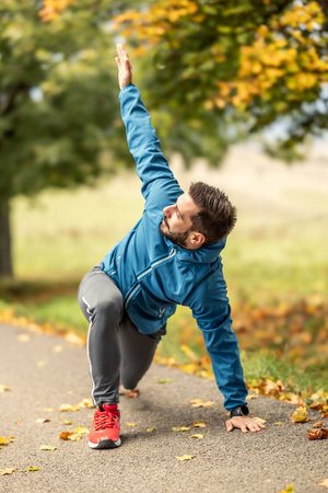 A young athlete is warming up before running training in the park. It warms the upper and lower part of the body.の写真素材