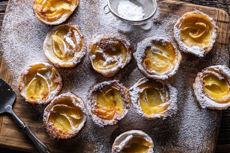 Mini tarts made of puff pastry and sliced apples sprinkled with powdered sugar on wooden cutting...