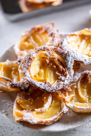 Mini tarts made of puff pastry and sliced apples sprinkled with powdered sugar on white plate....