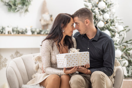 Happy couple look into each other's eyes holding a Christmas present together.の写真素材
