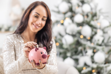 Woman saving money for Christmas while putting a two euro coin into a piggy bank.の写真素材