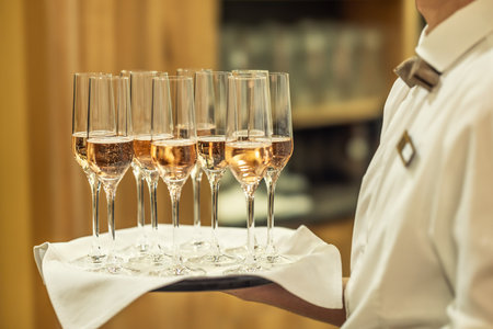 A young waiter holds a plate with champagne or prosecco as a welcome drink at a hotel event.の写真素材