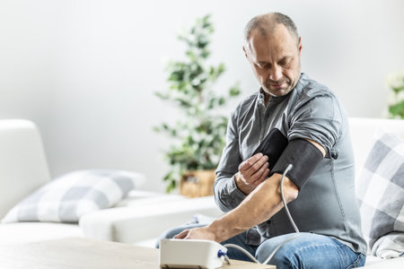 A mature man checking his blood pressure with a digital blood pressure monitor at home.の写真素材