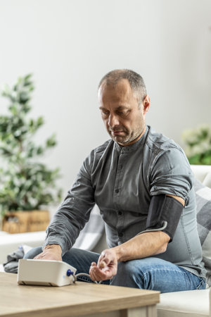 A mature man checking his blood pressure with a digital blood pressure monitor at home.の写真素材