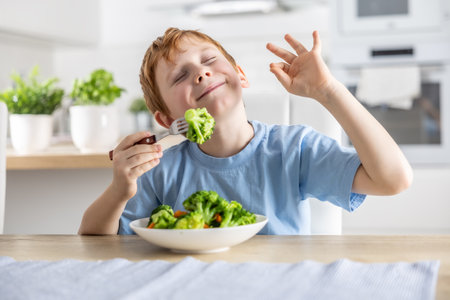 A cute little boy is eating broccoli for lunch and he likes it very much.の写真素材