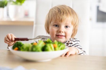 Cute little girl is eating broccoli and carrot vegetables with a fork.の写真素材