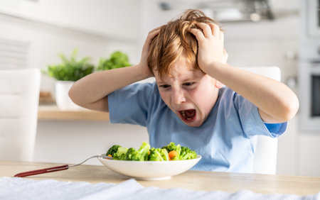 Shocked and upset little boy because he has to eat broccoli for dinner, which he doesn't like.の写真素材