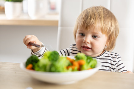 Cute little girl is eating broccoli and carrot vegetables with a fork.の写真素材
