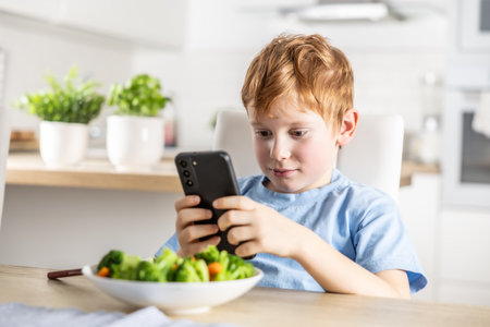 View of smart cute boy using smartphone before lunch in kitchen at home.の写真素材