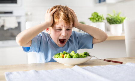 Shocked and upset little boy because he has to eat broccoli for dinner, which he doesn't like.の写真素材