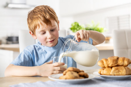 A little boy pours himself fresh milk during breakfast.の写真素材