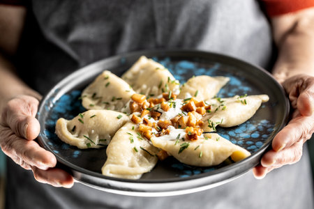 The hands of a senior home cook hold a plate with a national Slovak dish - Bryndzove Pirohy.