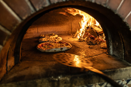 Traditional oven for baking pizza with burning wood and shovel. The cook rotates the pizza in the...
